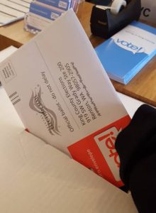 A hand slips a red King County Elections ballot envelop into a drop box.