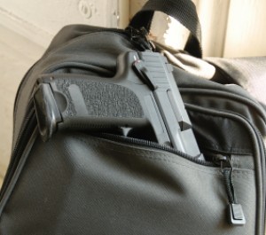 A black handgun rests part way in the front pocket of a black backpack