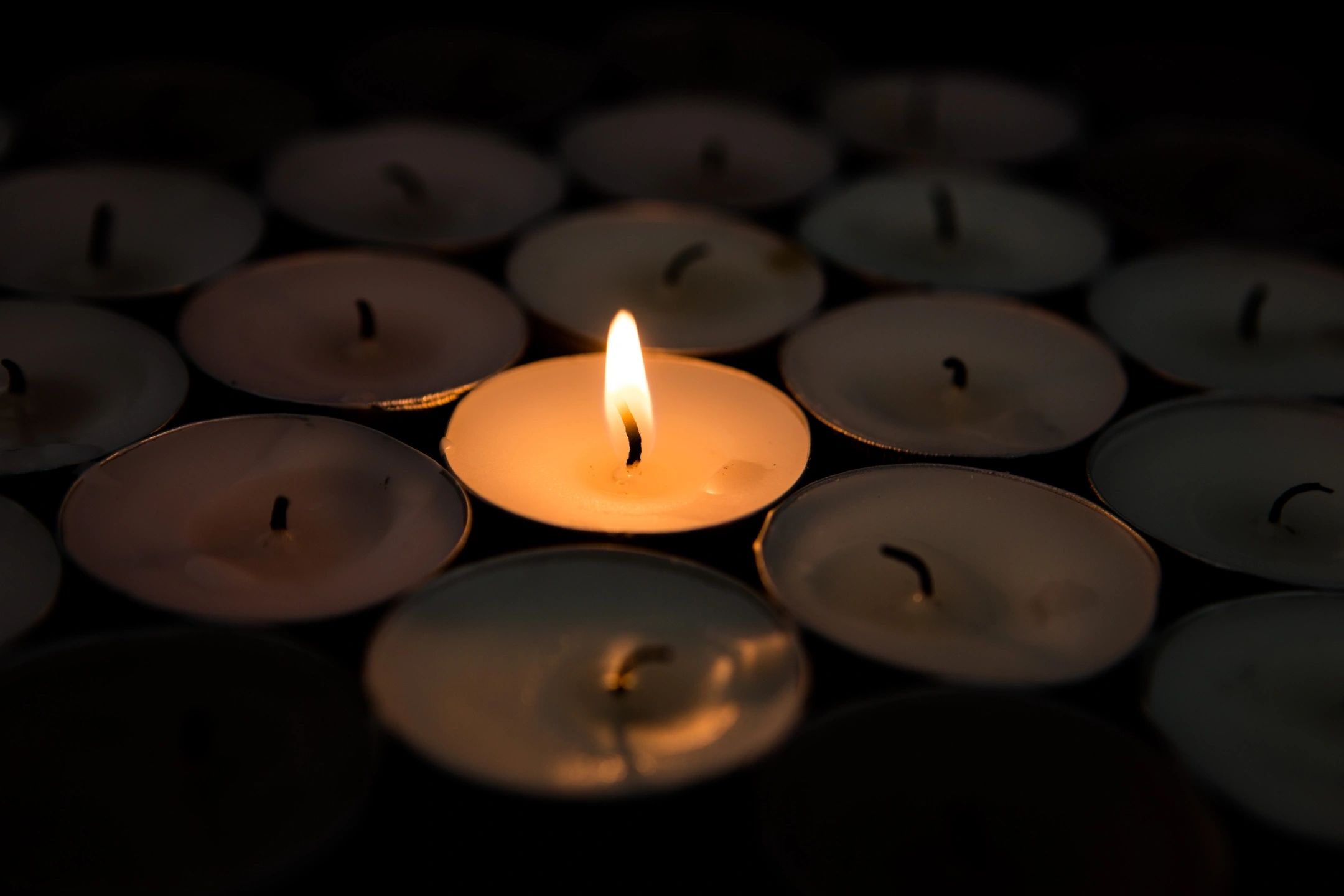a single lit tealight candle issurrounded by unlit tealight candles