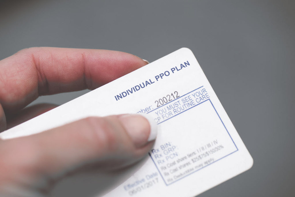 An insurance card is held between the thumb and index of what appears to be a female's hand. The nail of the thumb rests next to the group number of the Individual pro plan .