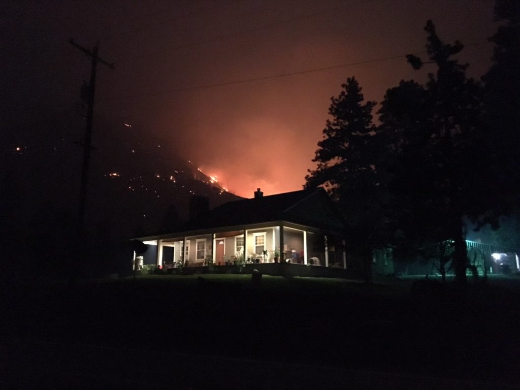 A home sits in the foreground of a looming wildfire
