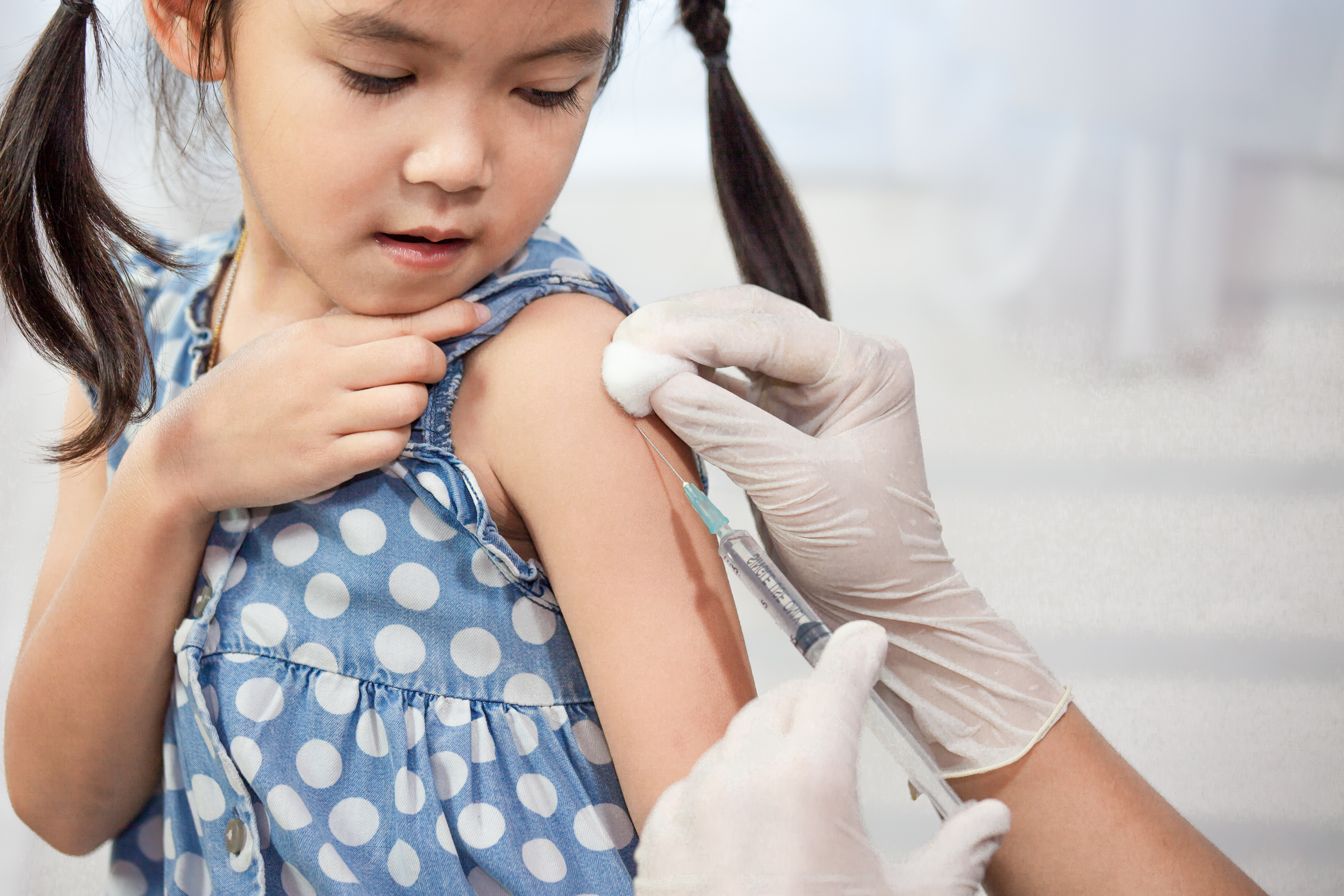 A young girl holds up her sleeve as she receives a vaccine shot