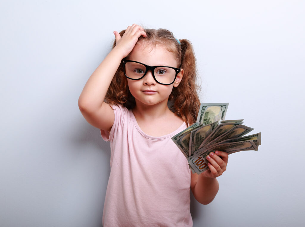 A female child holds a fanned out money with a confused look on her face