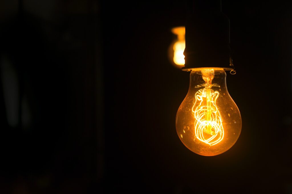 Two yellow hued lightbulbs hang to the right of an otherwise black photo
