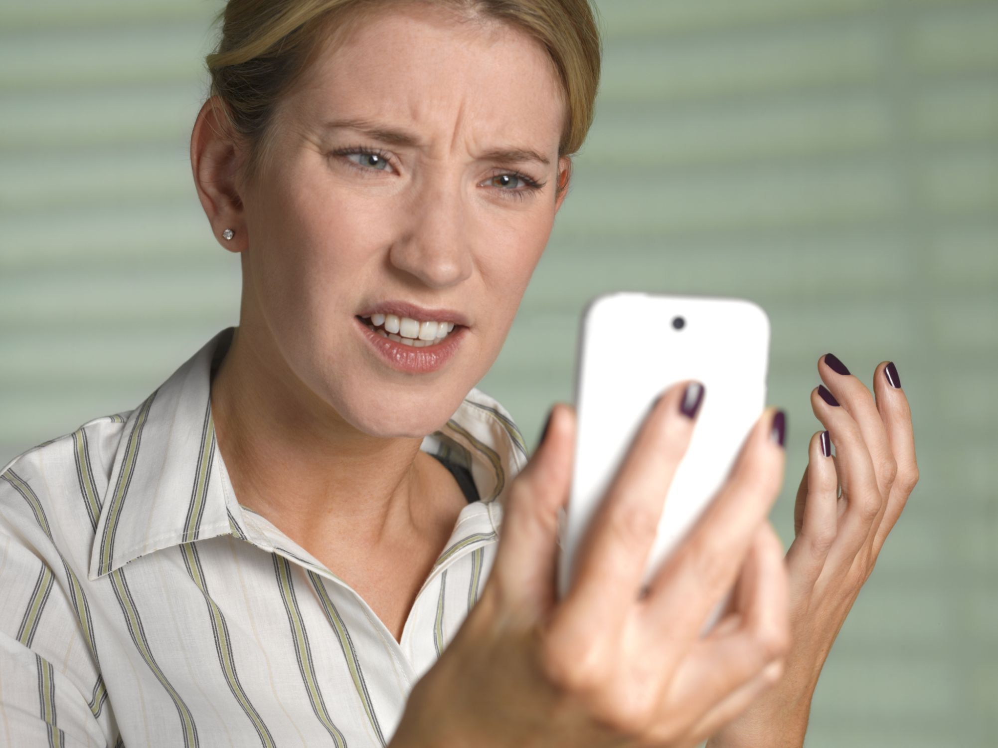 A blonde middle aged woman looks annoyed and confused at a white cellphone