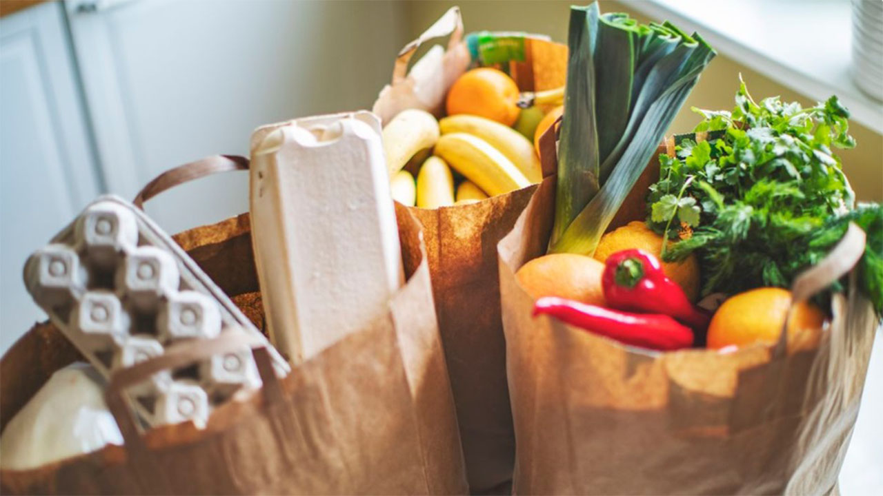 Three paper grocery bags full of colorful fruits, vegetables and other staple foods