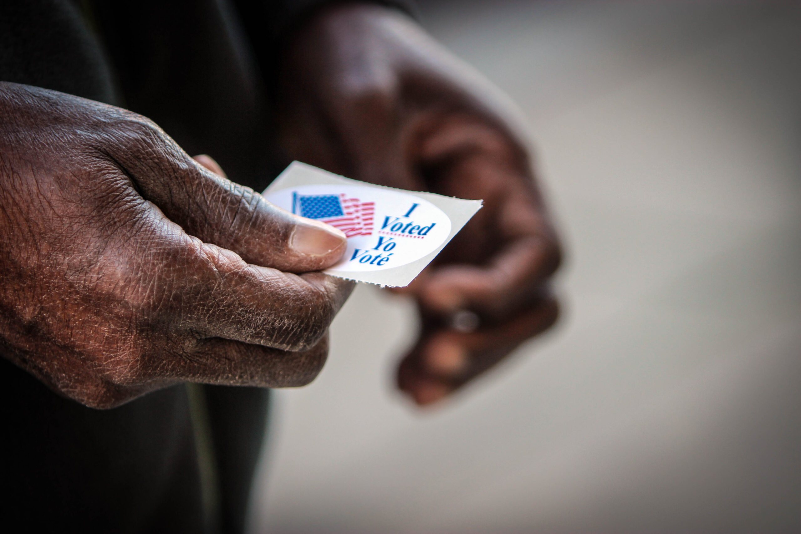 A photo of a senior Black man's hands holding an I Voted sticker.