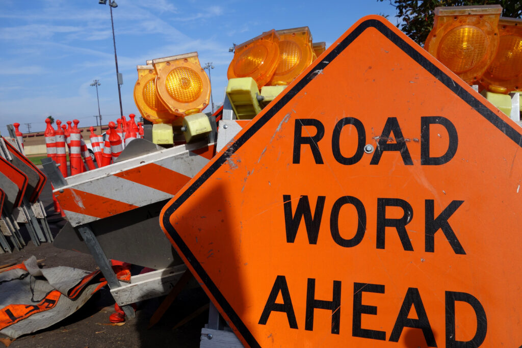 an orange road work ahead sign in front of stacked up temporary construction hurdles.