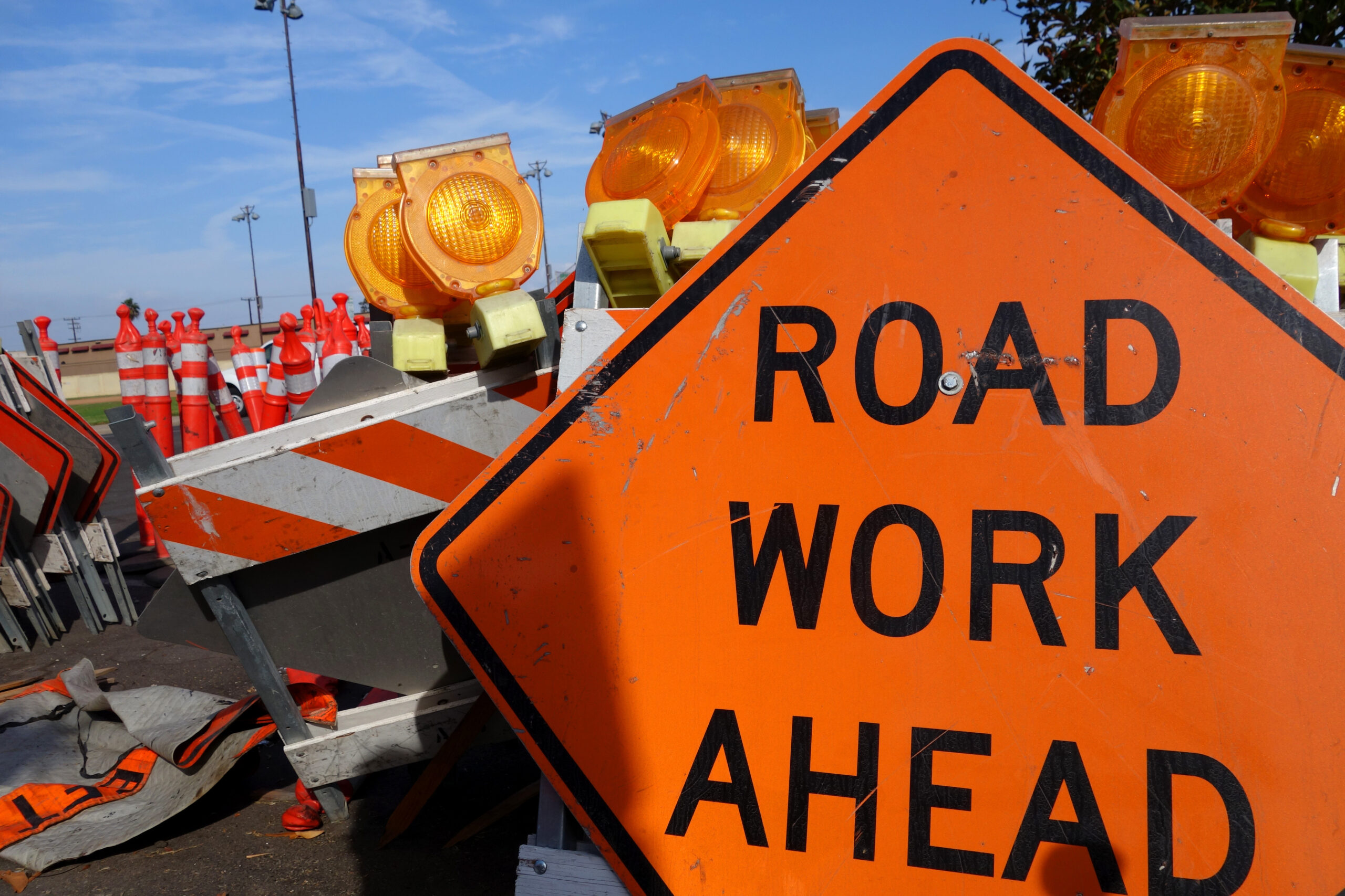 an orange road work ahead sign in front of stacked up temporary construction hurdles.