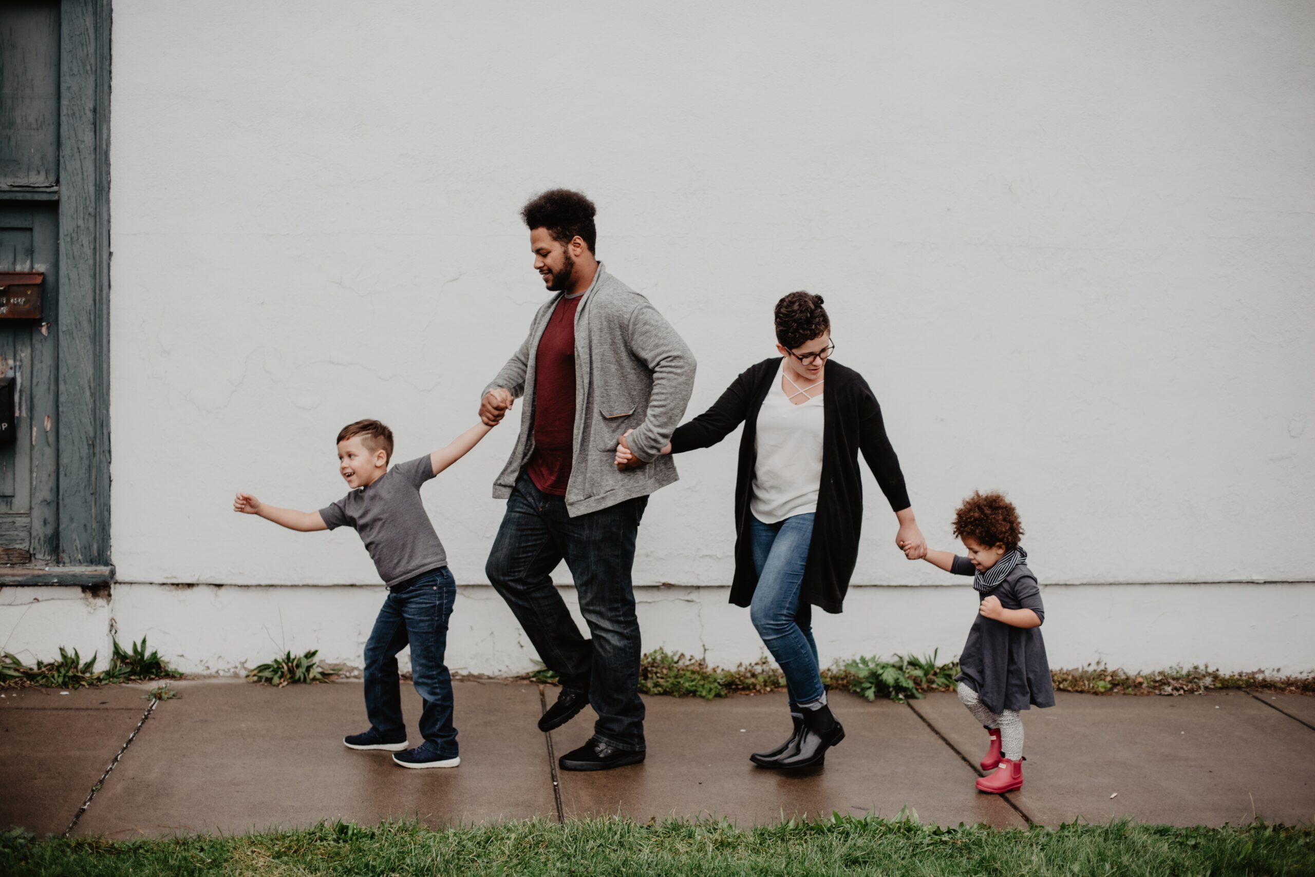 a family with two children walk in a line holding hands on a wet sidewalk