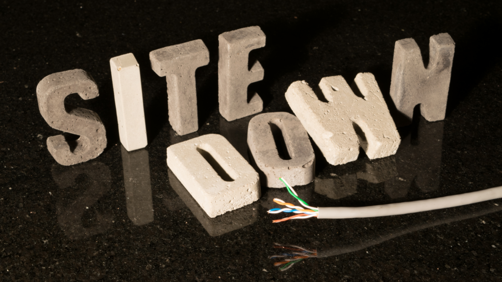 White stone letters on a reflective black top say "site down" The Down are fallen, with a cut cable laying in front of it.