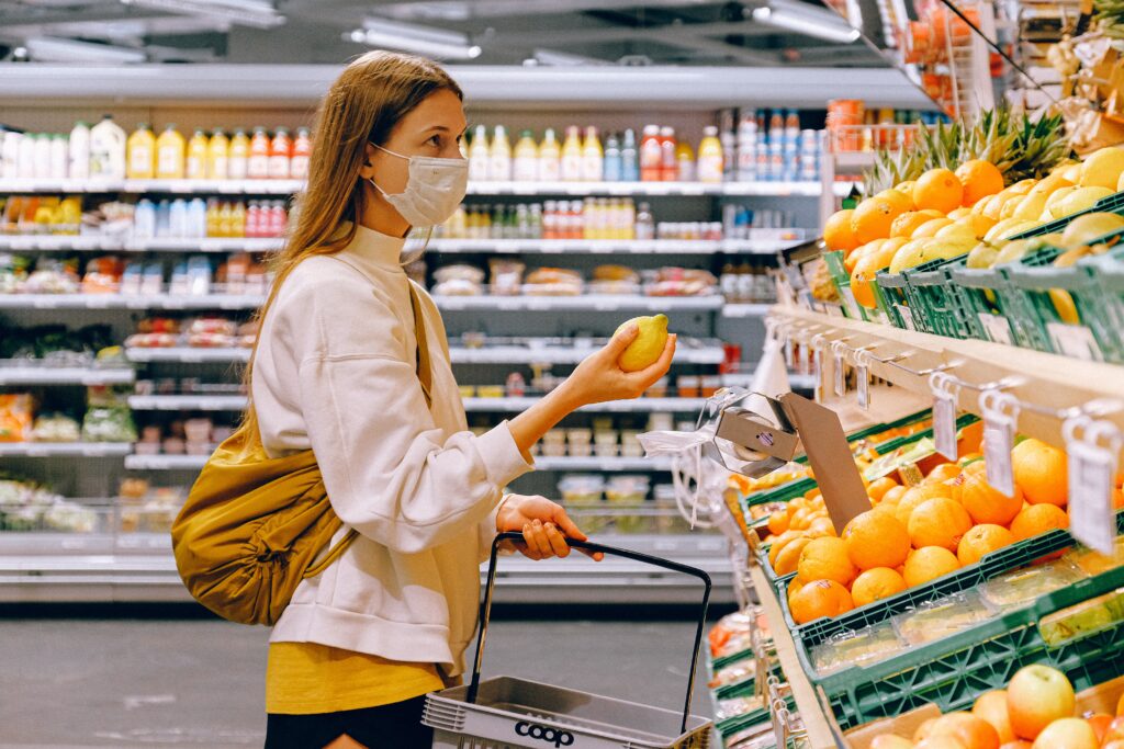 woman-in-yellow-tshirt-and-beige-jacket-holding-a-fruit in a grocery store