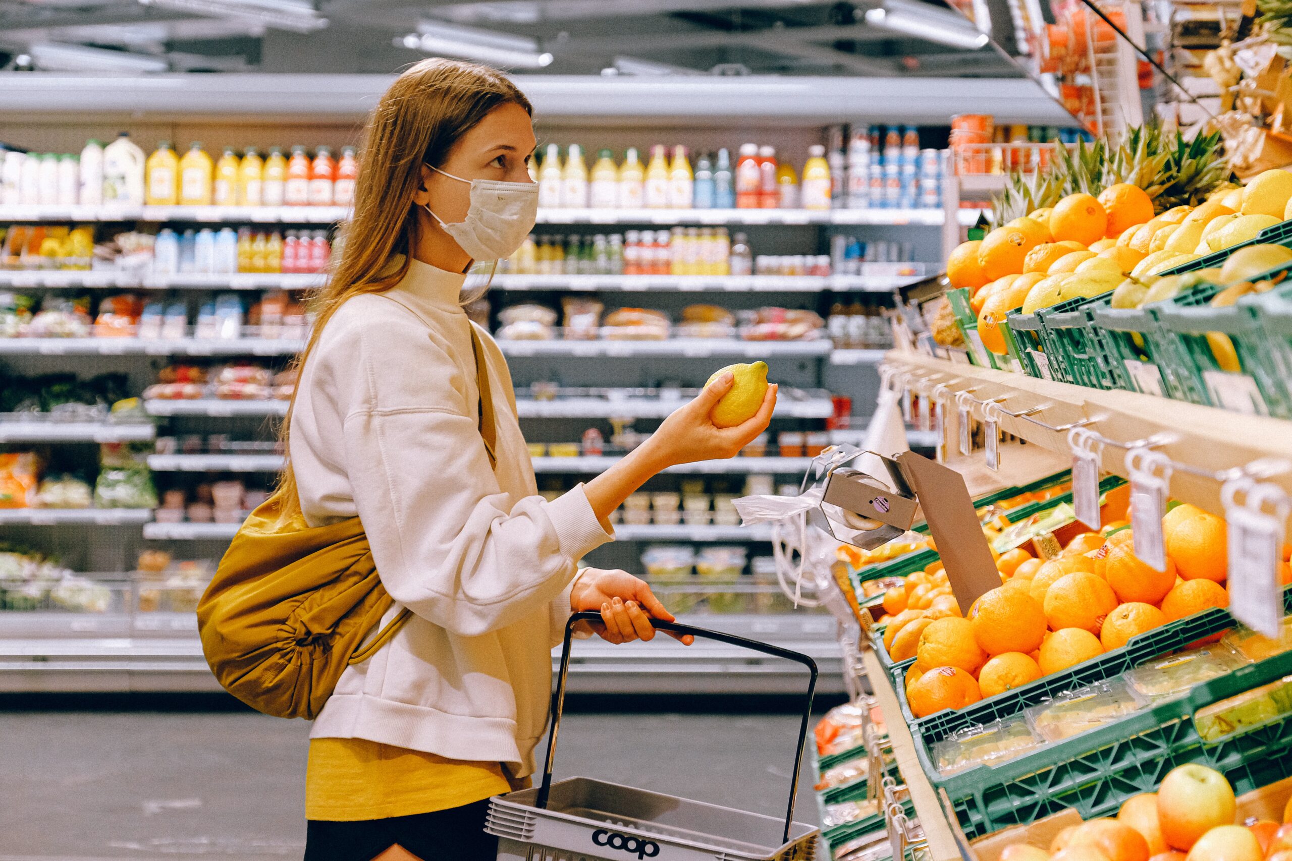 woman-in-yellow-tshirt-and-beige-jacket-holding-a-fruit in a grocery store