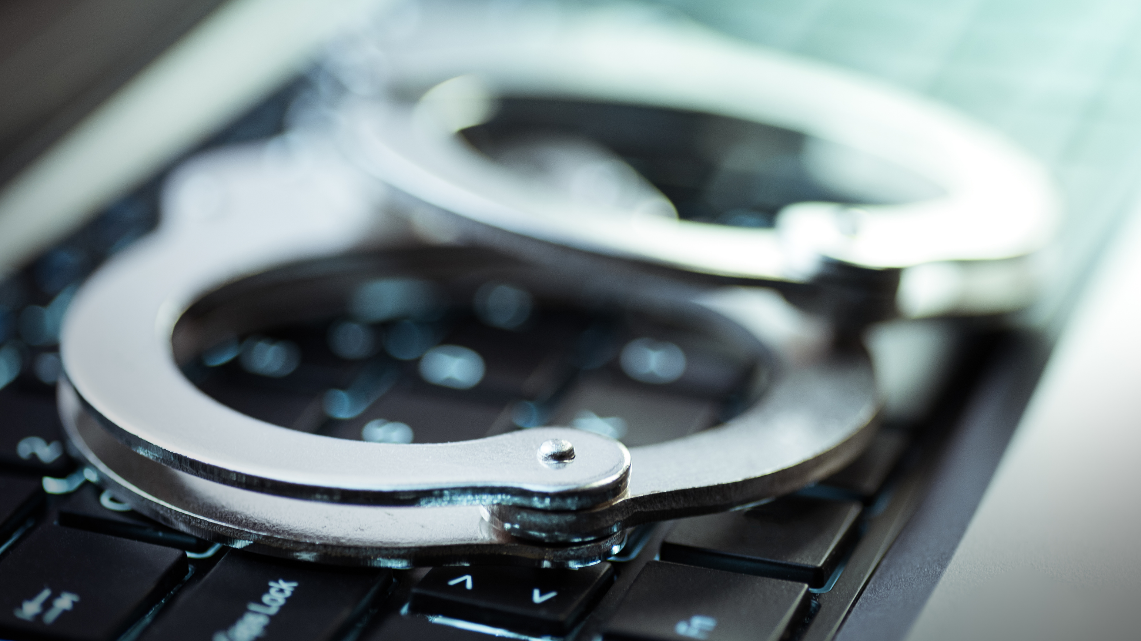 A pair of silver handcuffs on a black laptop keyboard