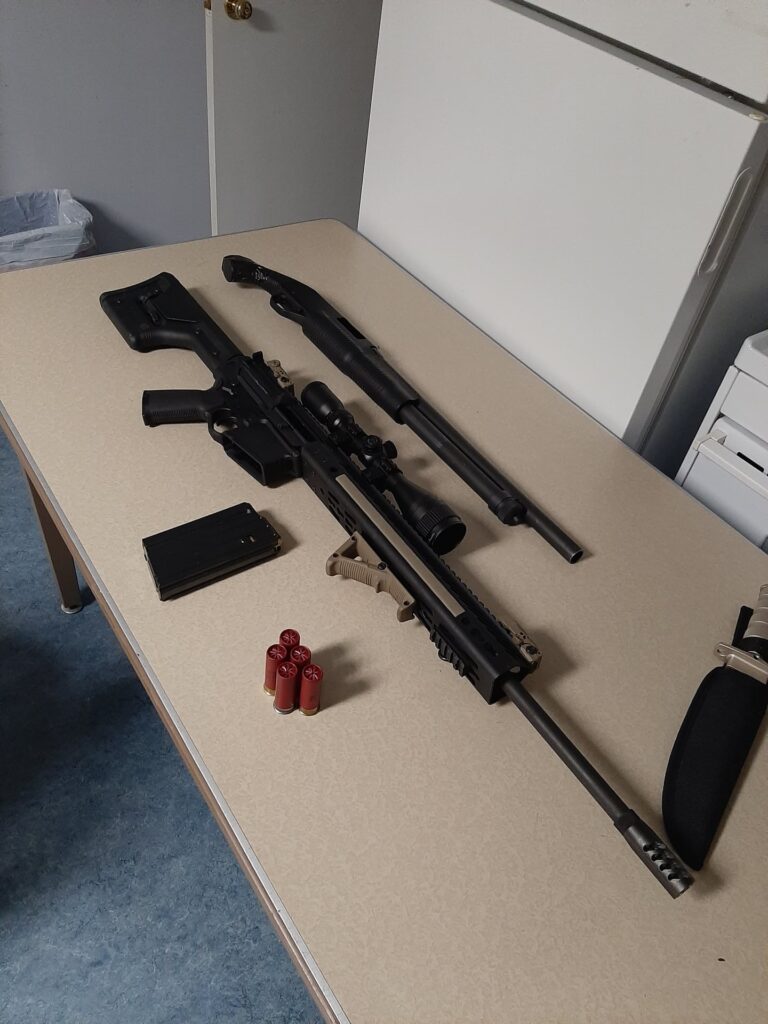 Firearms, a large knife, and ammunition lay on a table.