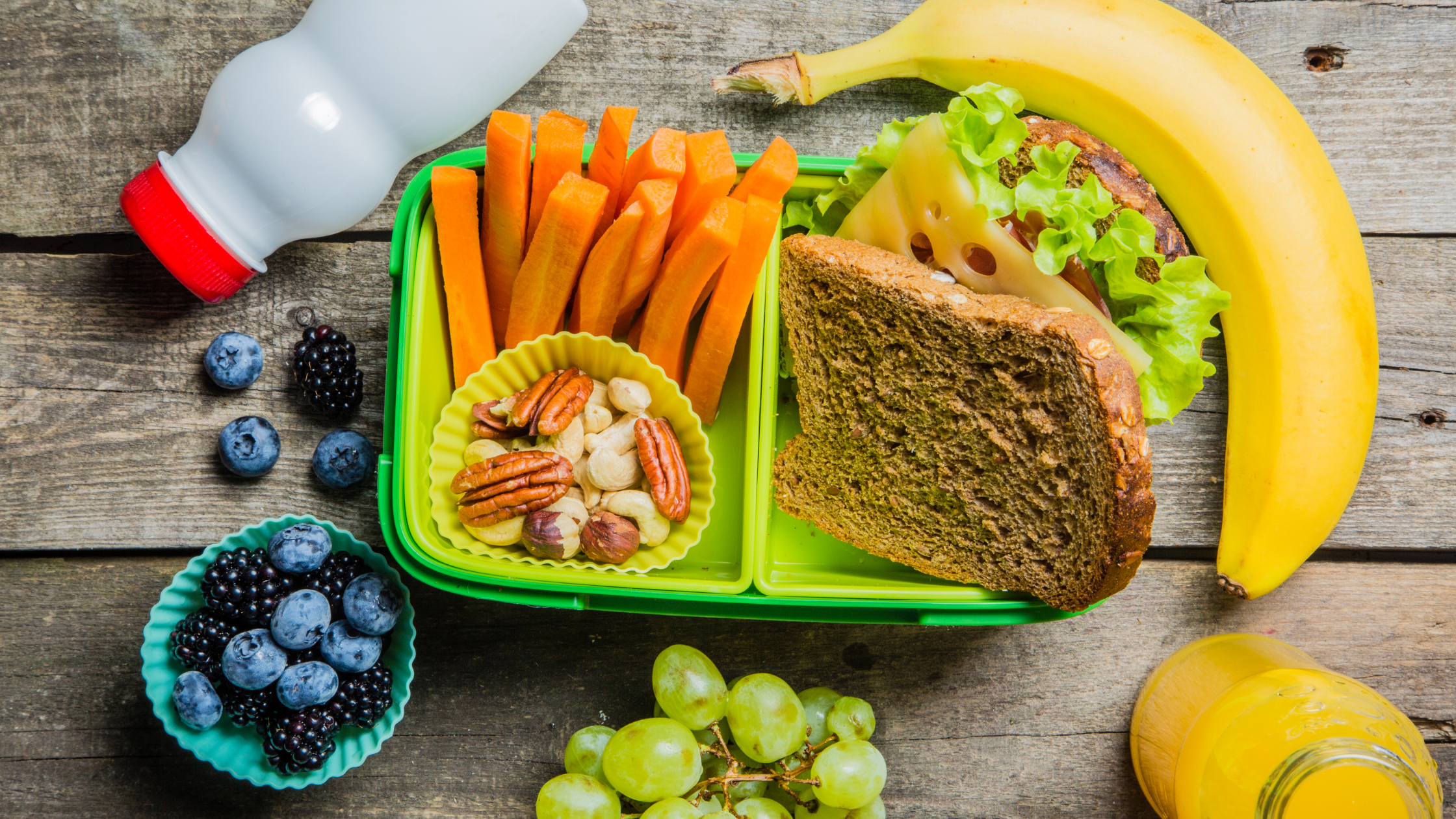 A healthy kid's lunch consisting of a sandwich, fruit, carrots and milk