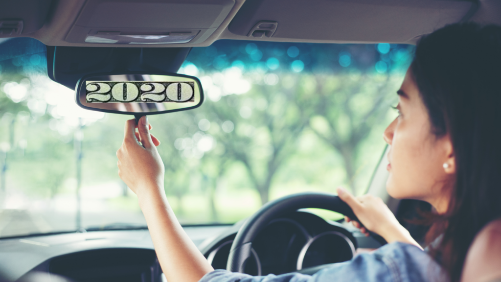 a woman looks in her rearview mirror, the number 2020 reflecting back at her