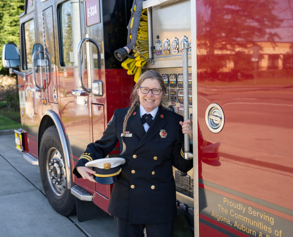 Fire Marshal Karen Stewart stands next to a fire truck in her dress uniform.