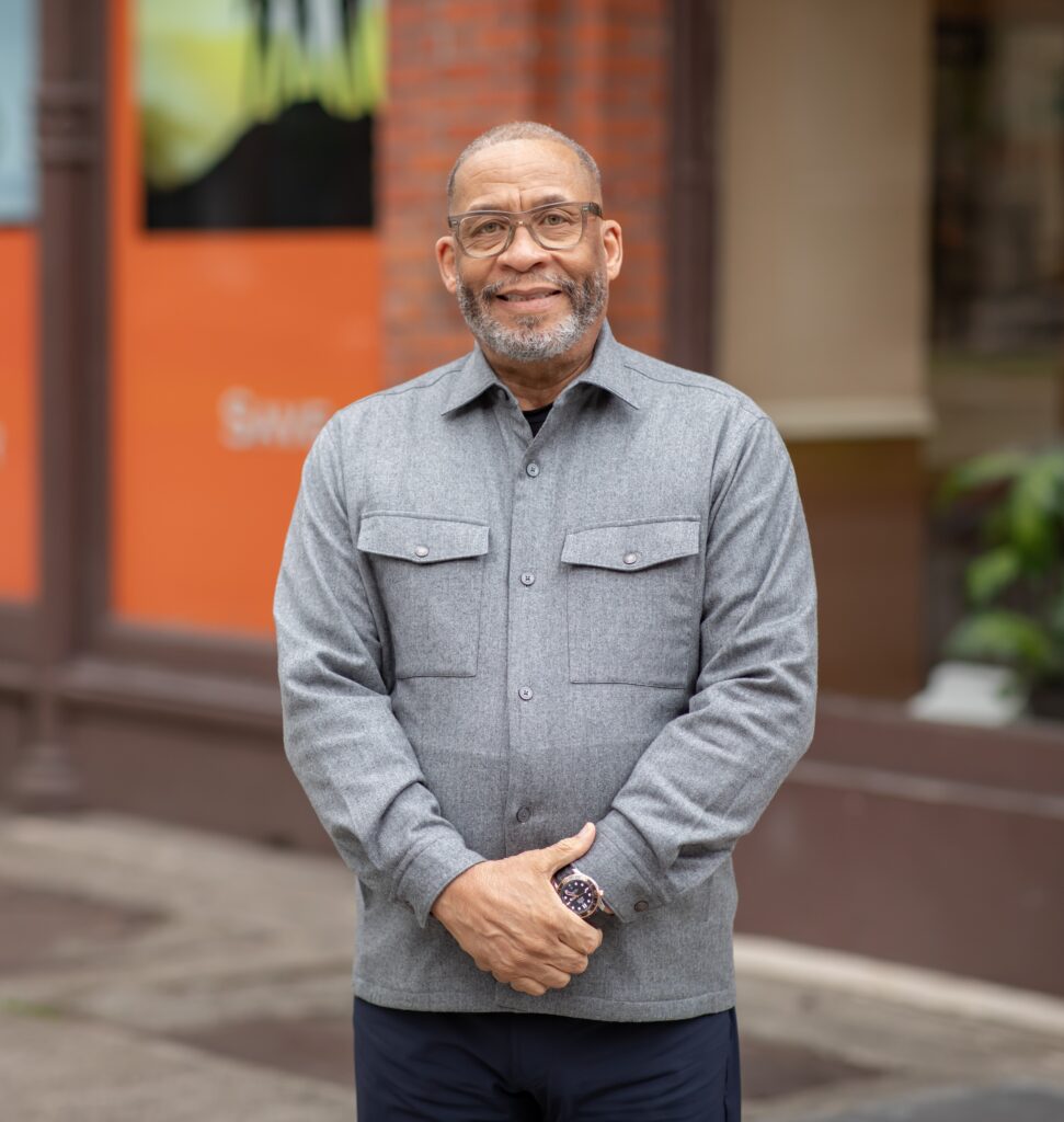 Willie Parish, an older Black man of medium height and build, stands with his arms in front of his waist.