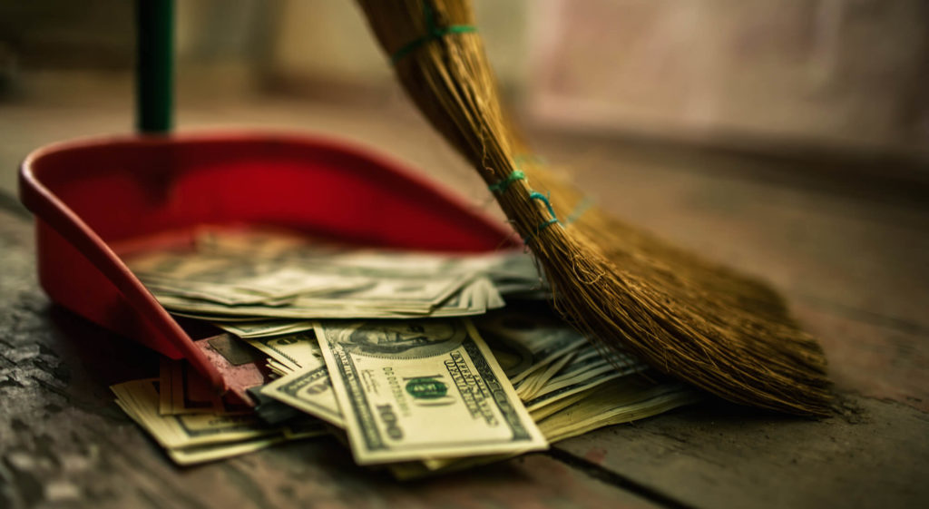 a broom sweeps 100 dollar bills into a red dustpan