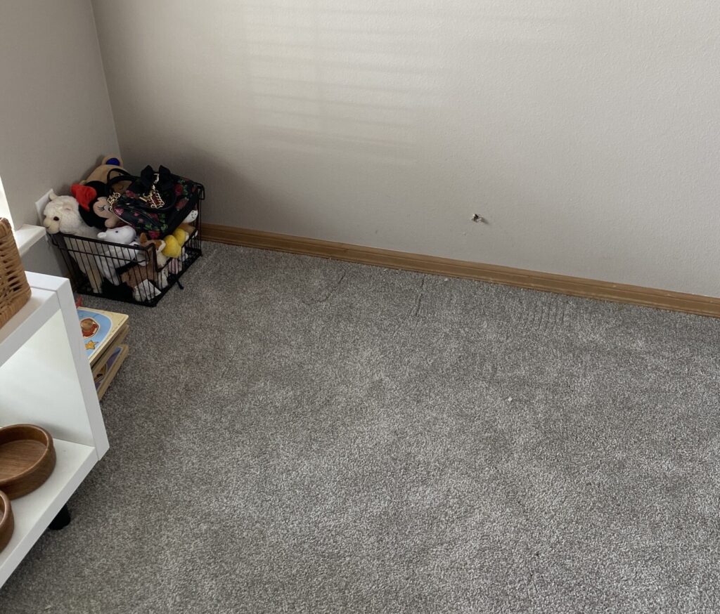 The corner of a room, a small hole near the bottom of the wall shown. To the left of the photo children's toys can be seen.