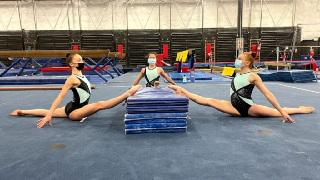 three Ascend gymnastics gymnasts do splits with their front lets lifted onto a stack of mats