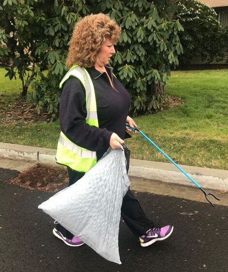Auburn Mayor Nancy Backus picks up litter with a grabber and trash bag on a street in Auburn