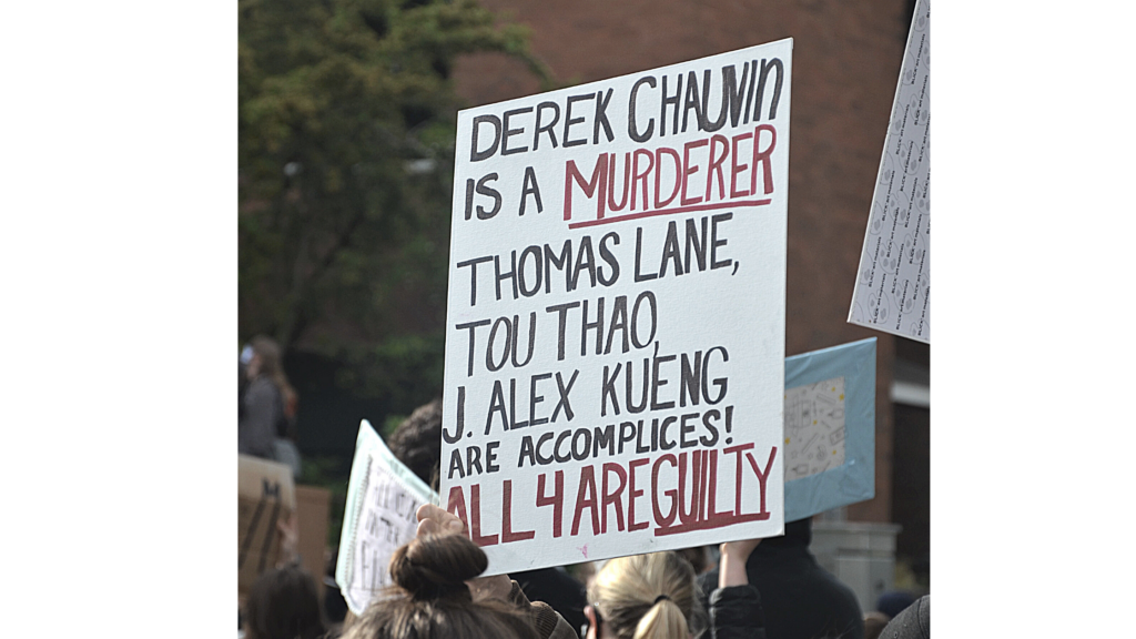 A protester holds a sign up at the June 3 Auburn BLM rally. the sign reads "Derek Chaubin is a Murderer. Thomas Lane, Tou Thoa, J. Alex Kueing are accomplices. All 4 are guilty"