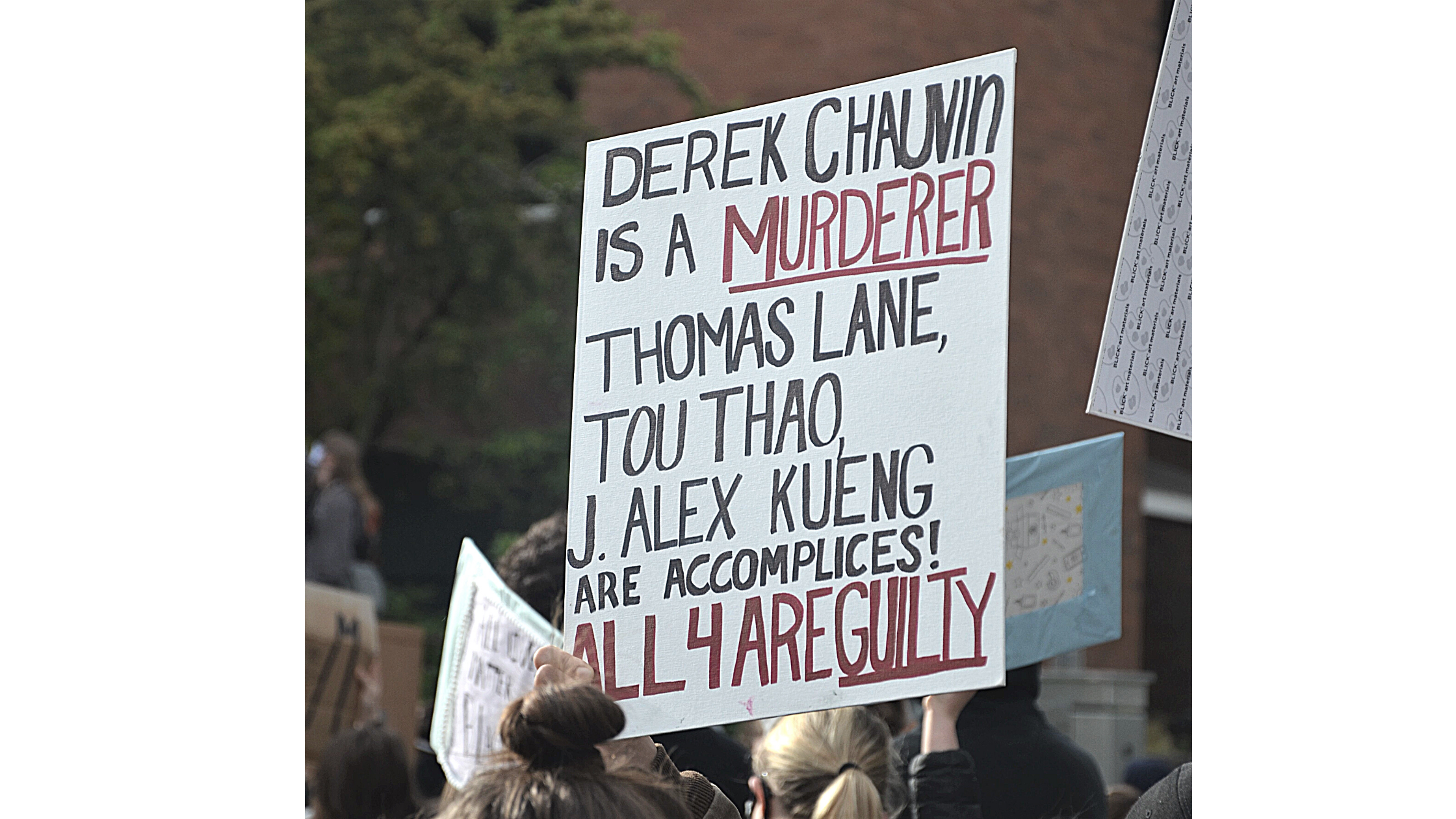 A protester holds a sign up at the June 3 Auburn BLM rally. the sign reads "Derek Chaubin is a Murderer. Thomas Lane, Tou Thoa, J. Alex Kueing are accomplices. All 4 are guilty"