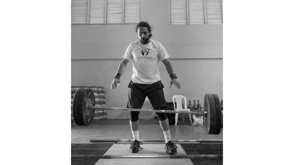 A black and white photo of Harrison Maurus, a large barbell falling to the ground in front of him.
