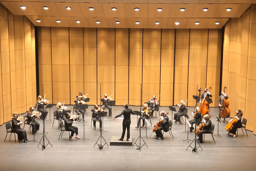The symphony orchestra, spaced apart, plays on a stage