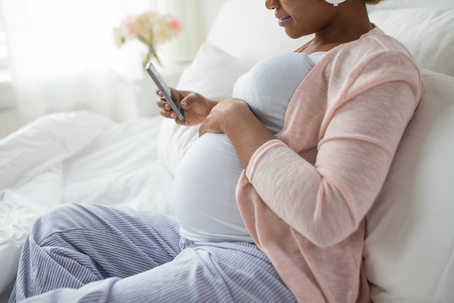 Close up of pregnant African American woman with smartphone in bed at home