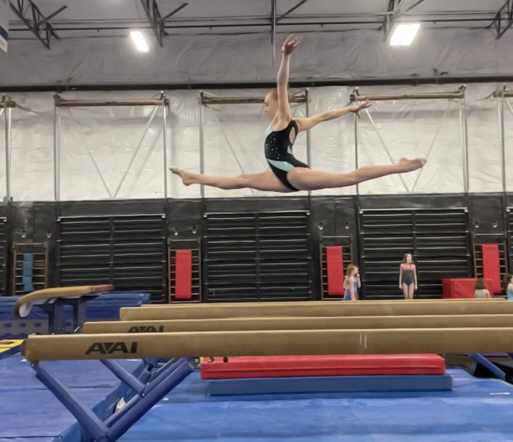 Isabelle Futch is captured mid-air doing the splits on the balance beam at Ascend Gymnastics