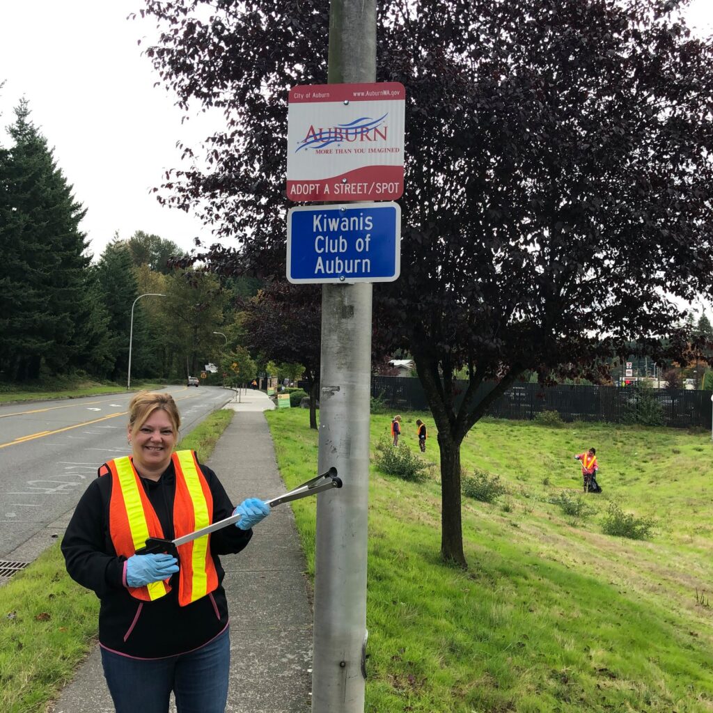 A Kiwanis member stands under the service group's Adopt-a-Street sign while holding a garbage grabber.