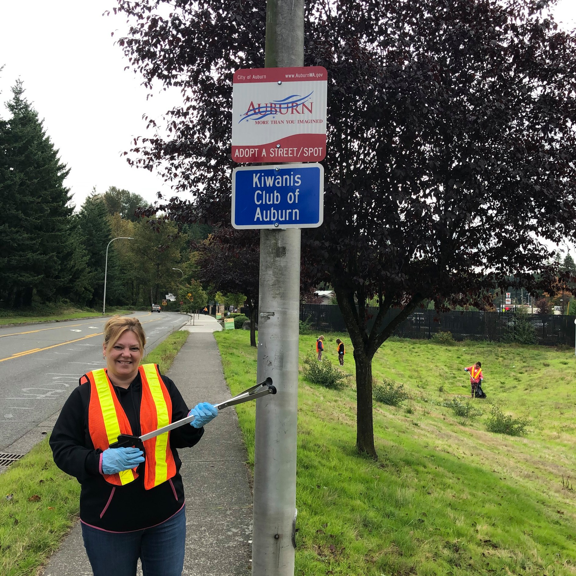 A Kiwanis member stands under the service group's Adopt-a-Street sign while holding a garbage grabber.