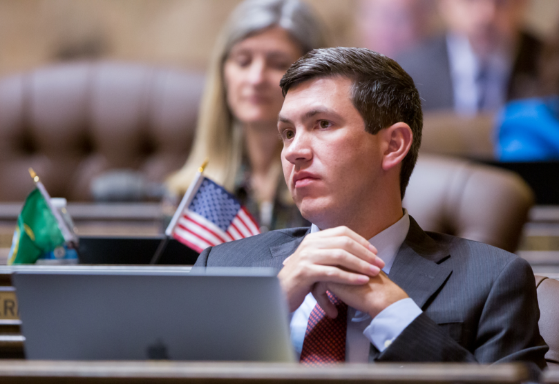 Rep. Drew Stokesbary of Auburn leans back in his chair at his desk in the State House chamber. his hands folded at his chest in front of him. Stokesbary looks off to the side with a concerned expression