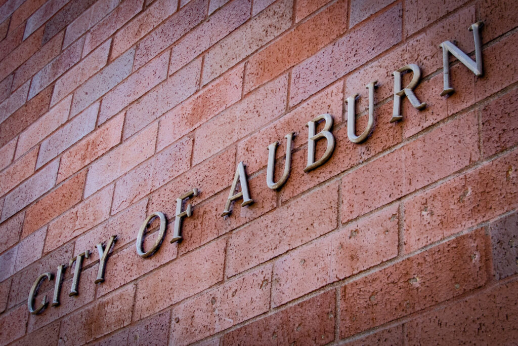 a metal "City of Auburn" sign on a red brick wall