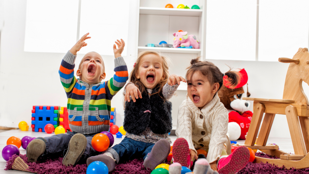 three toddler age children laugh in a daycare setting