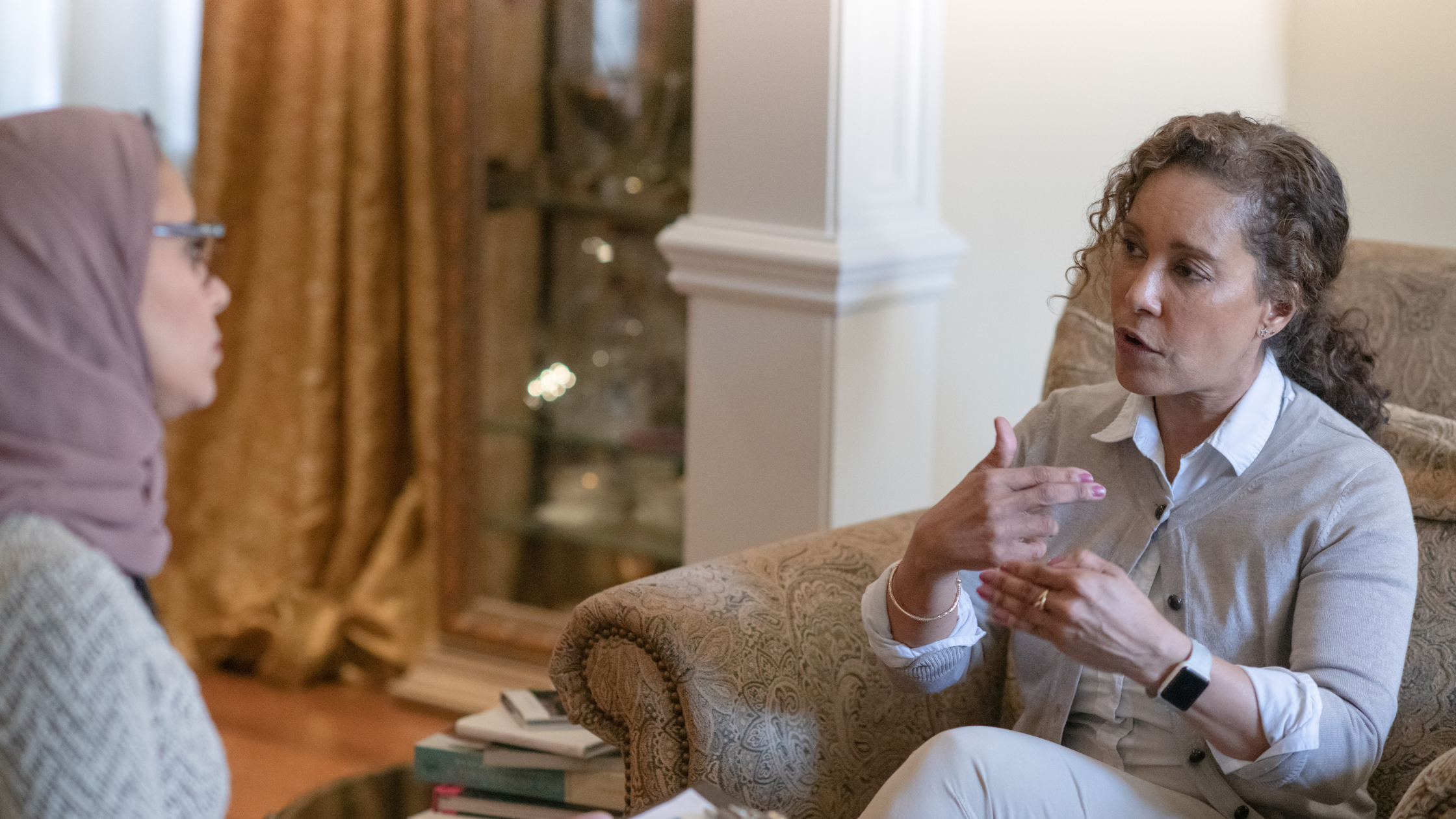 two women sit across from each other speaking. The implication of the photo is they are in a therapy session.