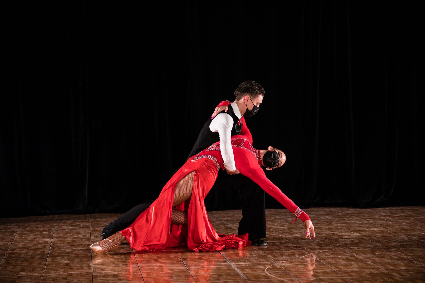 A male dancer holds a female dancer as he dips her back, her arm extending out toward the ground