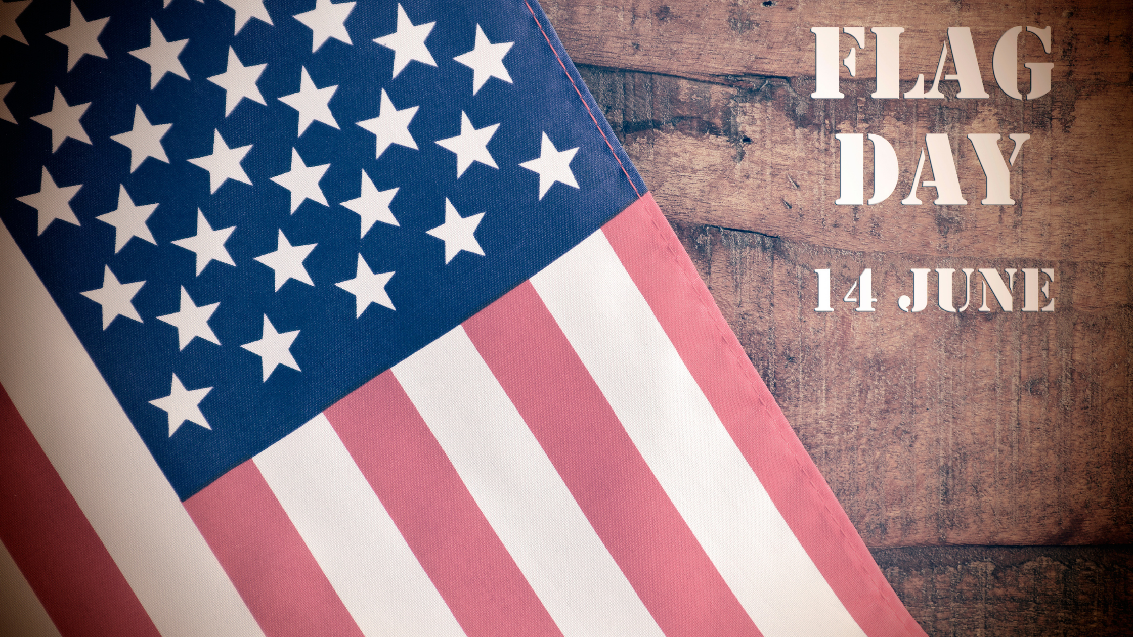 an American flag drapes over a wood background Flag Day June 14 is overlayed on the image
