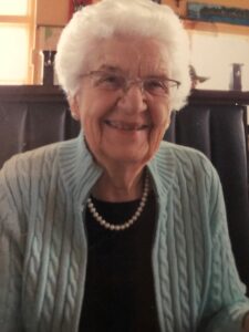 A photograph of an elderly White female sitting in a chair, smiling.