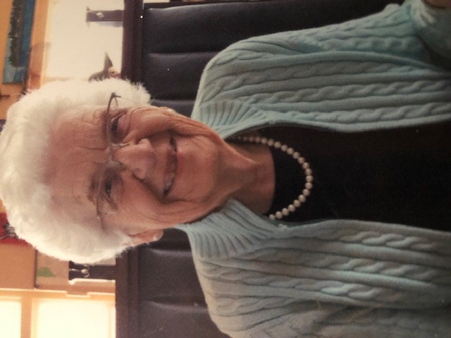 A photograph of an elderly White female sitting in a chair, smiling.