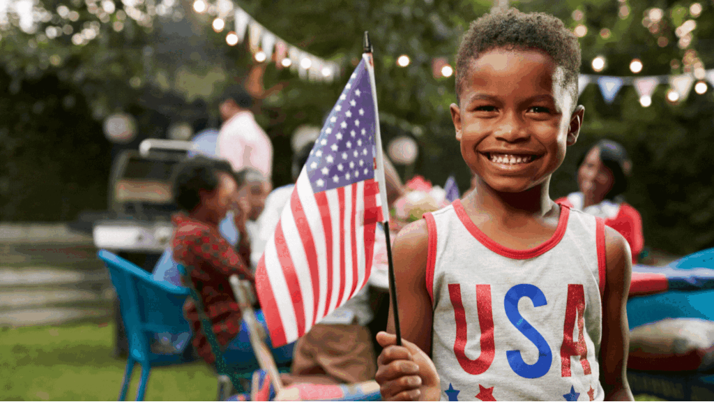 A little boy wearing a USA shirt holds an amaerican flag while at a family picnic