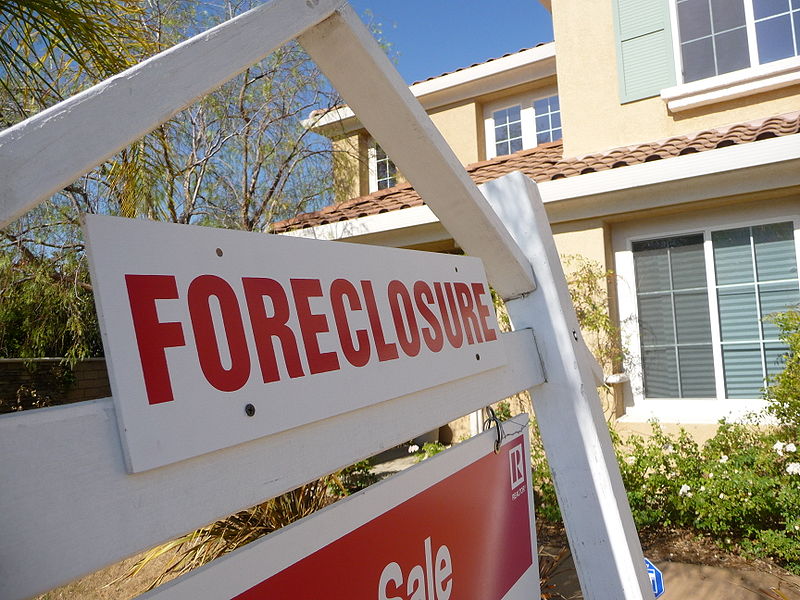 An up close photo of a real estate foreclosure sign in front of a single family home