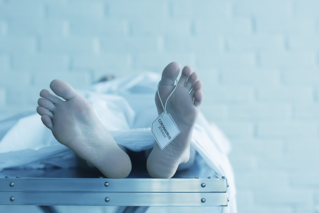 male covered on table in morgue, his feet sticking out with toe tag that reads "coronavirus 2019"