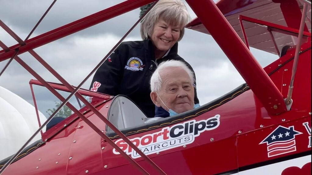 Darrell Campbell sits in a restored biplane with a female smiling behind him