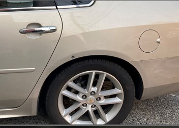 The back panel of a gold impala with a bullet hole over the rear tire