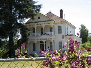 A historic farmhouse, Neely Mansion, with flowers along a chainlink fence in the foreground.