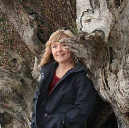A photo headshot of poet Cindy Hutchings standing by a tree